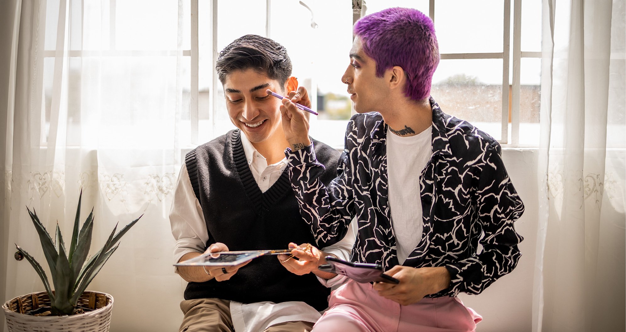 Cosmetic Services - two people sitting next to each other, one is putting make up on the other ones face, one has pink hair