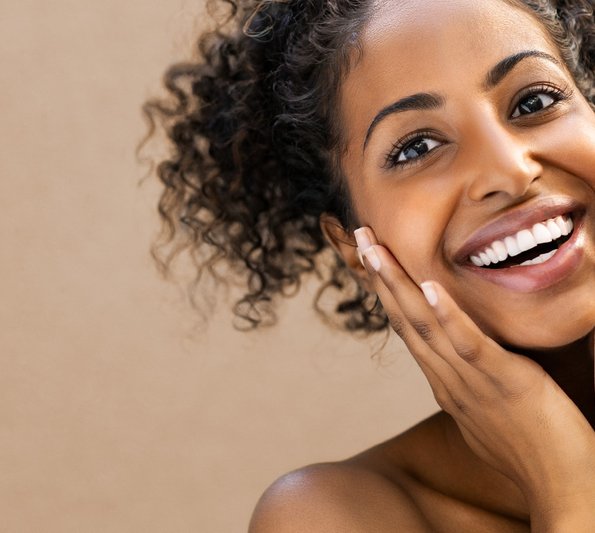 Rahn cosmetic news - young woman with dark skin and curly hair holding her hands against her cheeks