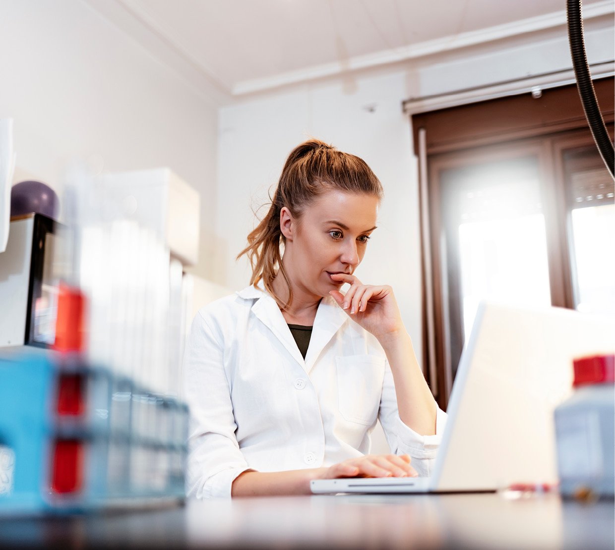 Cosmetic Services - young woman in a lab in front of her computer, holding her hand against her chin while thinking