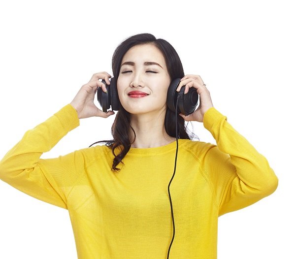 cosmetic actives trends - young asian woman wearing headphones and a yellow sweater